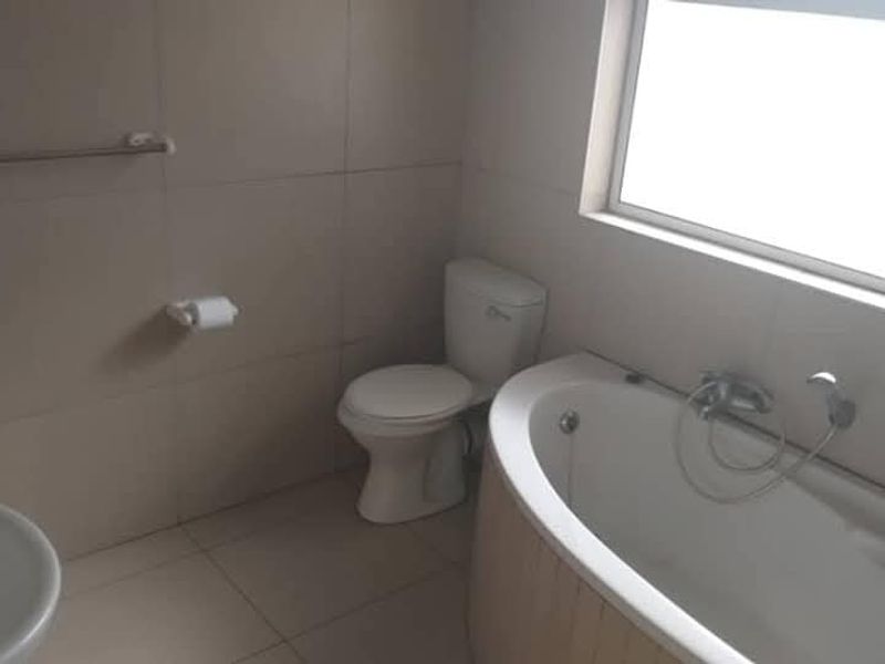 A functional bathroom featuring a bathtub with a handheld shower mixer, a toilet, and a wall-mounted basin, finished with neutral wall and floor tiles.