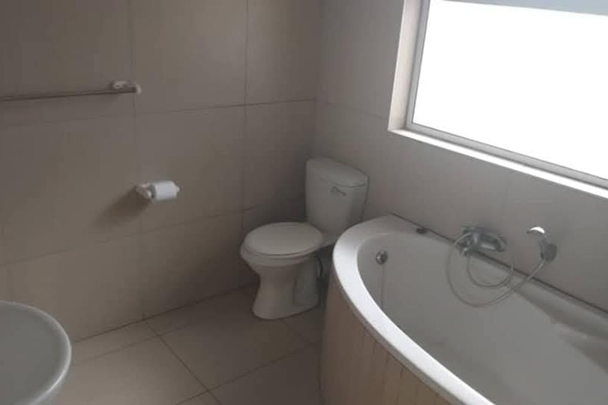 A functional bathroom featuring a bathtub with a handheld shower mixer, a toilet, and a wall-mounted basin, finished with neutral wall and floor tiles.