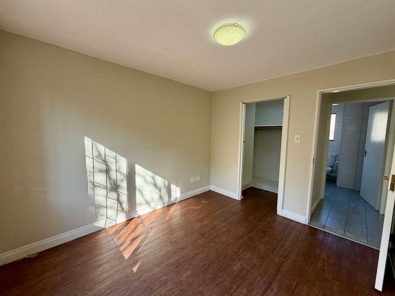 A vacant bedroom featuring laminate flooring, a built-in closet, and direct access to an en-suite bathroom.