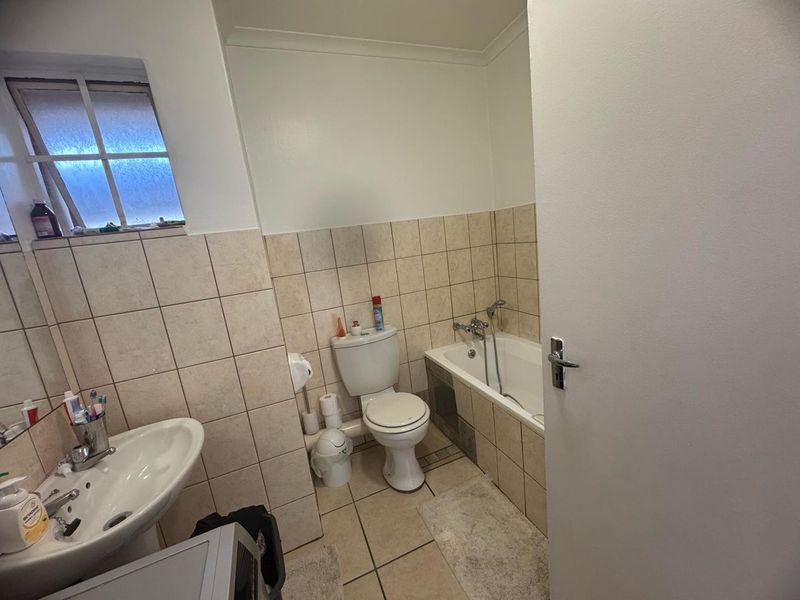A functional bathroom featuring a pedestal basin, toilet, and a bathtub with shower attachment, finished with neutral wall and floor tiling.