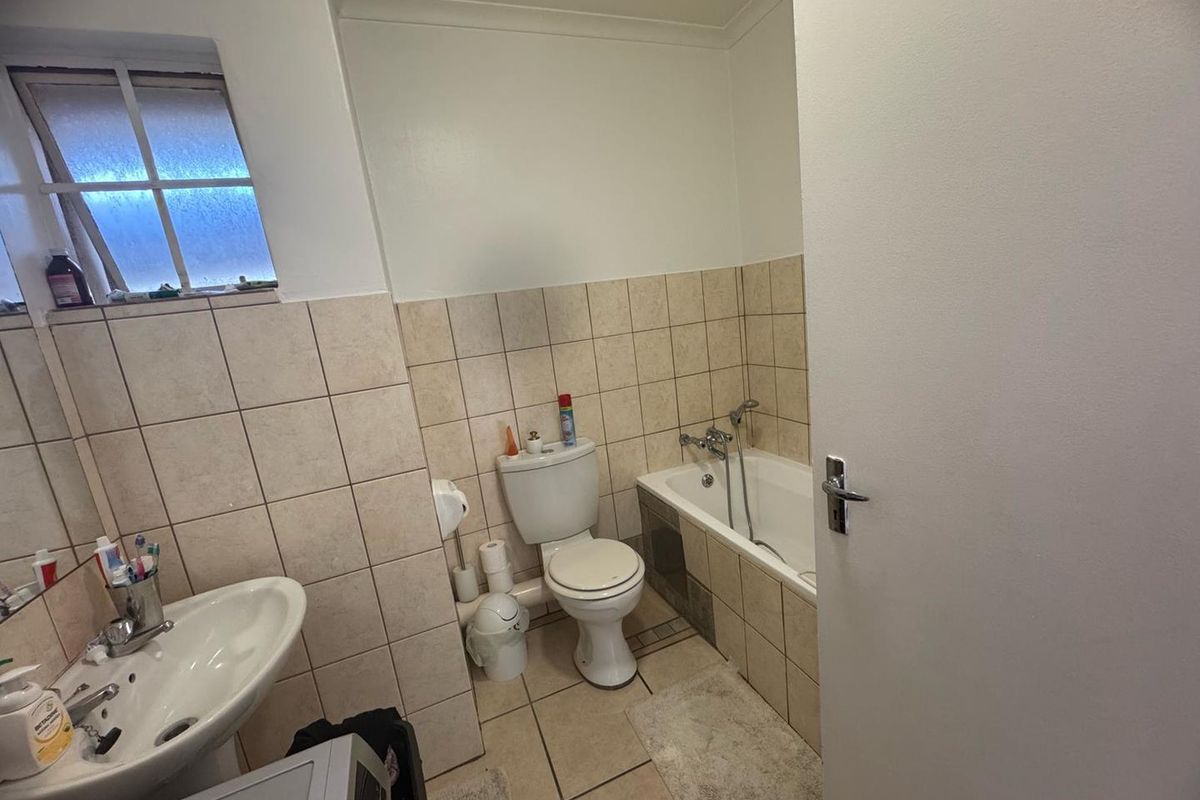 A functional bathroom featuring a pedestal basin, toilet, and a bathtub with shower attachment, finished with neutral wall and floor tiling.