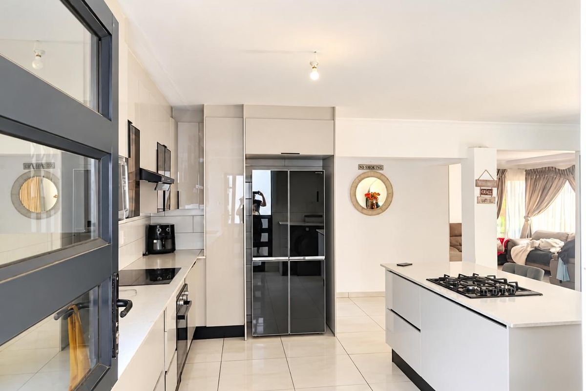 Modern kitchen featuring sleek cabinetry, stone countertops, a central island with a gas hob, and high-gloss tiled flooring.