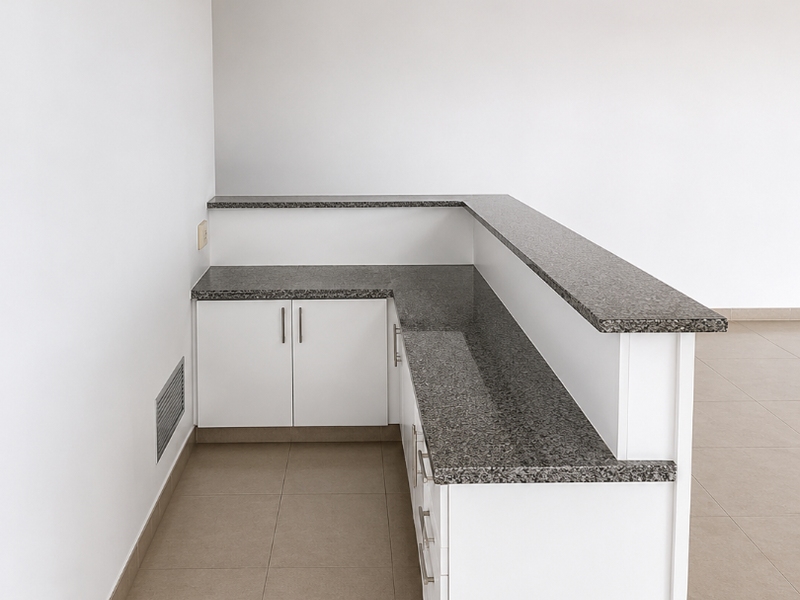 A clean, empty office space featuring a built-in reception desk with granite countertops, tiled flooring, and a professional drop ceiling with recessed lighting.