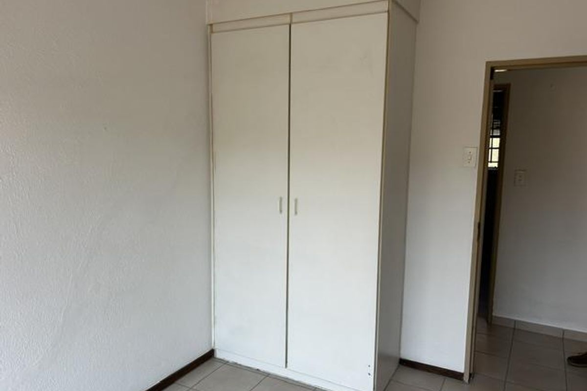 A simple bedroom featuring a built-in white wardrobe, tiled flooring, and neutral wall finishes.