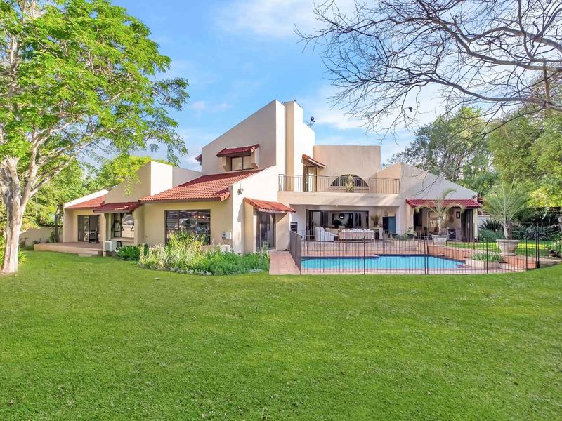 Rear view of a multi-level residence featuring a swimming pool, covered patio, balcony, and expansive landscaped garden.
