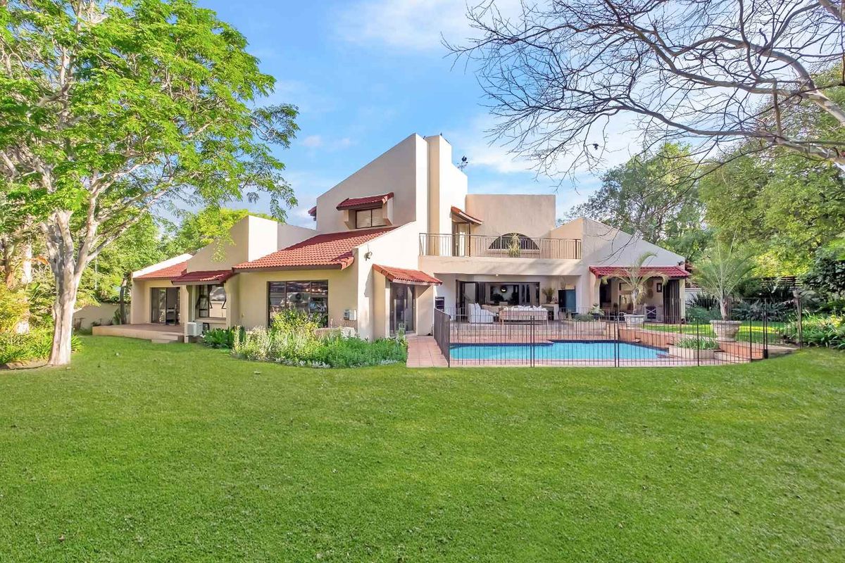 Rear view of a multi-level residence featuring a swimming pool, covered patio, balcony, and expansive landscaped garden.