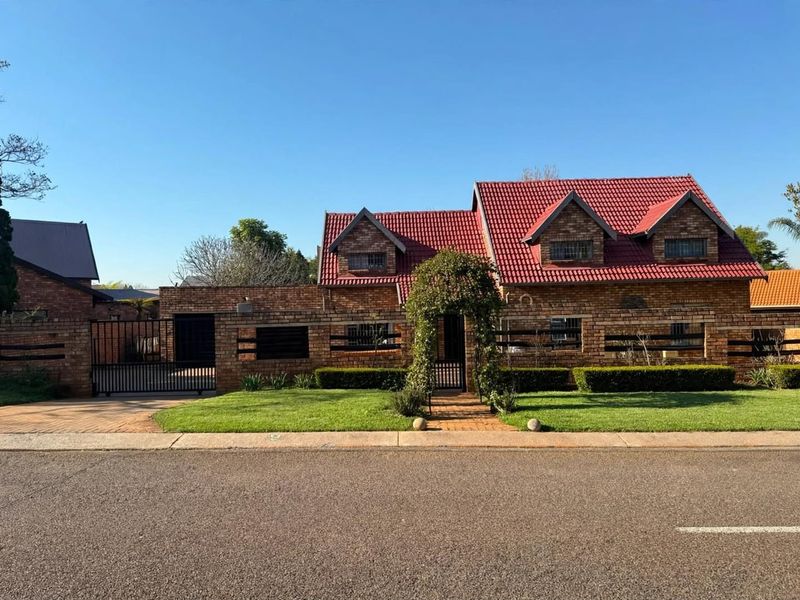 Front elevation of a face brick house featuring a red tiled roof, dormer windows, a paved driveway, and a manicured front garden.
