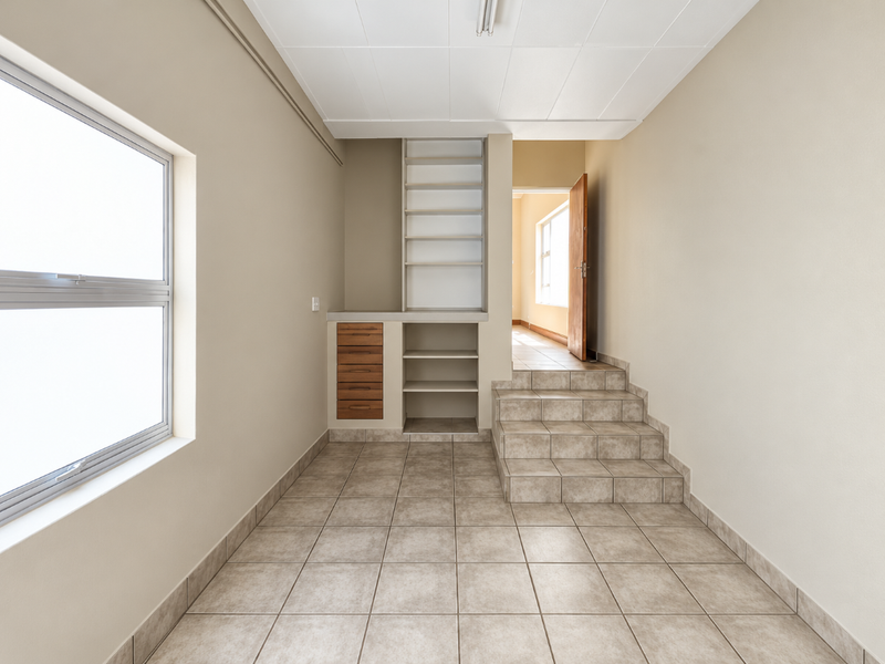 A bright, tiled hallway featuring built-in storage shelving and drawers, with a short staircase leading to an adjacent room.