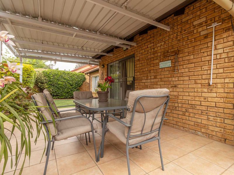 A covered outdoor patio area featuring tiled flooring and an exposed brick wall, providing a functional space for outdoor dining and relaxation.