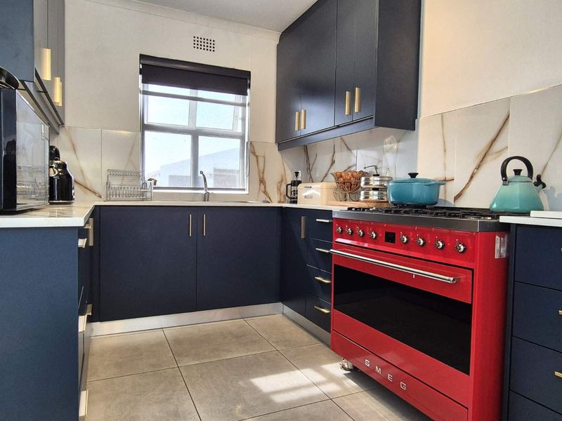 Modern kitchen featuring dark blue cabinetry, stone countertops, marble-look splashback, and a prominent red Smeg gas stove.