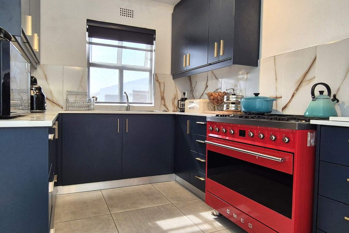 Modern kitchen featuring dark blue cabinetry, stone countertops, marble-look splashback, and a prominent red Smeg gas stove.