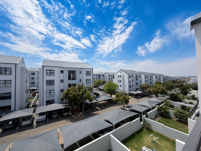 An elevated view of the apartment complex grounds, featuring multiple residential blocks, covered parking bays, and well-maintained communal garden areas.