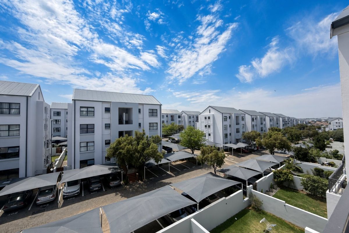 An elevated view of the apartment complex grounds, featuring multiple residential blocks, covered parking bays, and well-maintained communal garden areas.