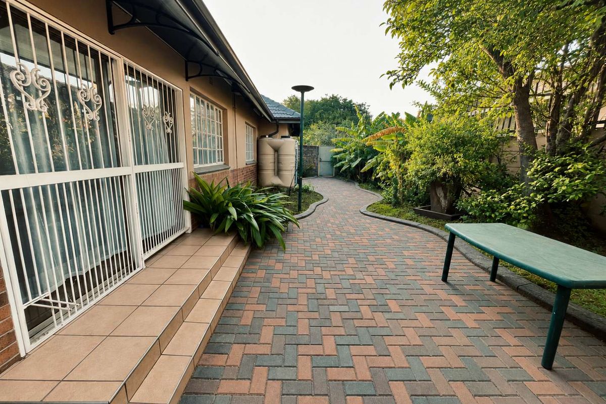 A well-maintained paved side walkway and patio area featuring security gates, a water tank, and established garden landscaping.