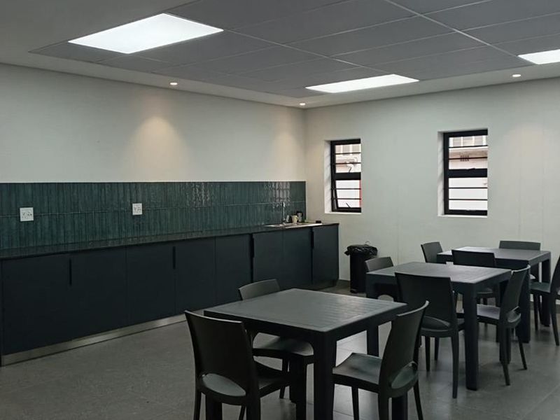A clean, modern industrial kitchen area featuring dark cabinetry, a tiled backsplash, and recessed lighting, suitable for office or commercial use.