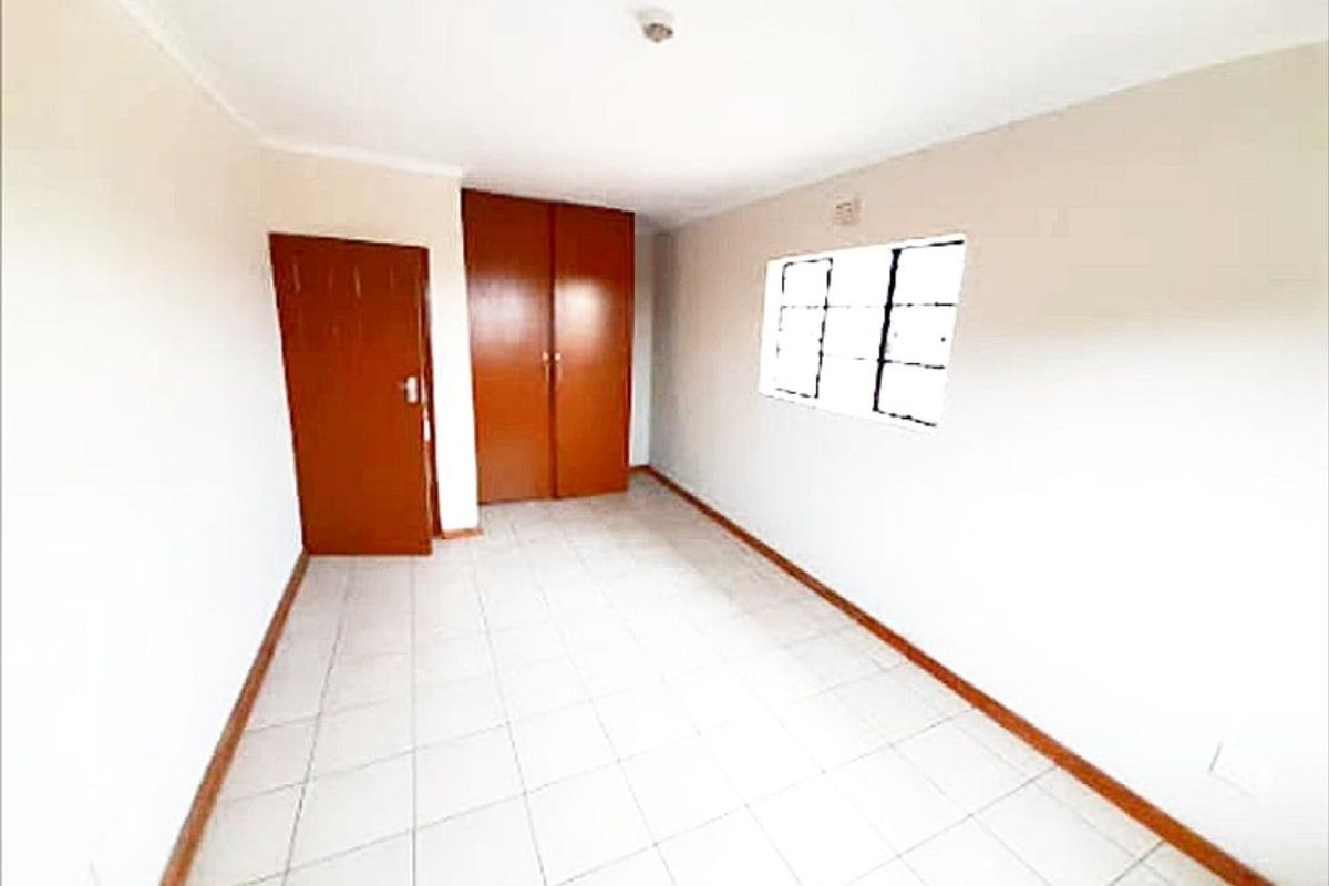 A clean, empty bedroom featuring tiled flooring, built-in wooden cupboards, and a window providing natural light.