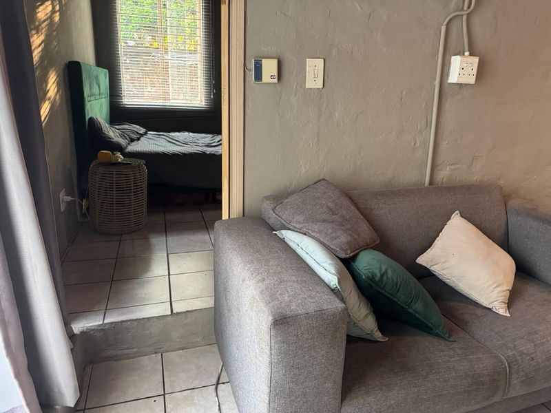 A living area featuring tiled floors and exposed electrical conduit, with a view into an adjacent bedroom space.