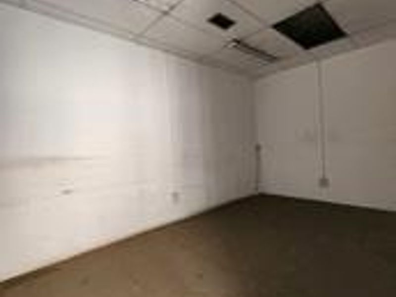 An empty, utilitarian office space featuring a suspended ceiling, fluorescent lighting, and worn finishes requiring refurbishment.