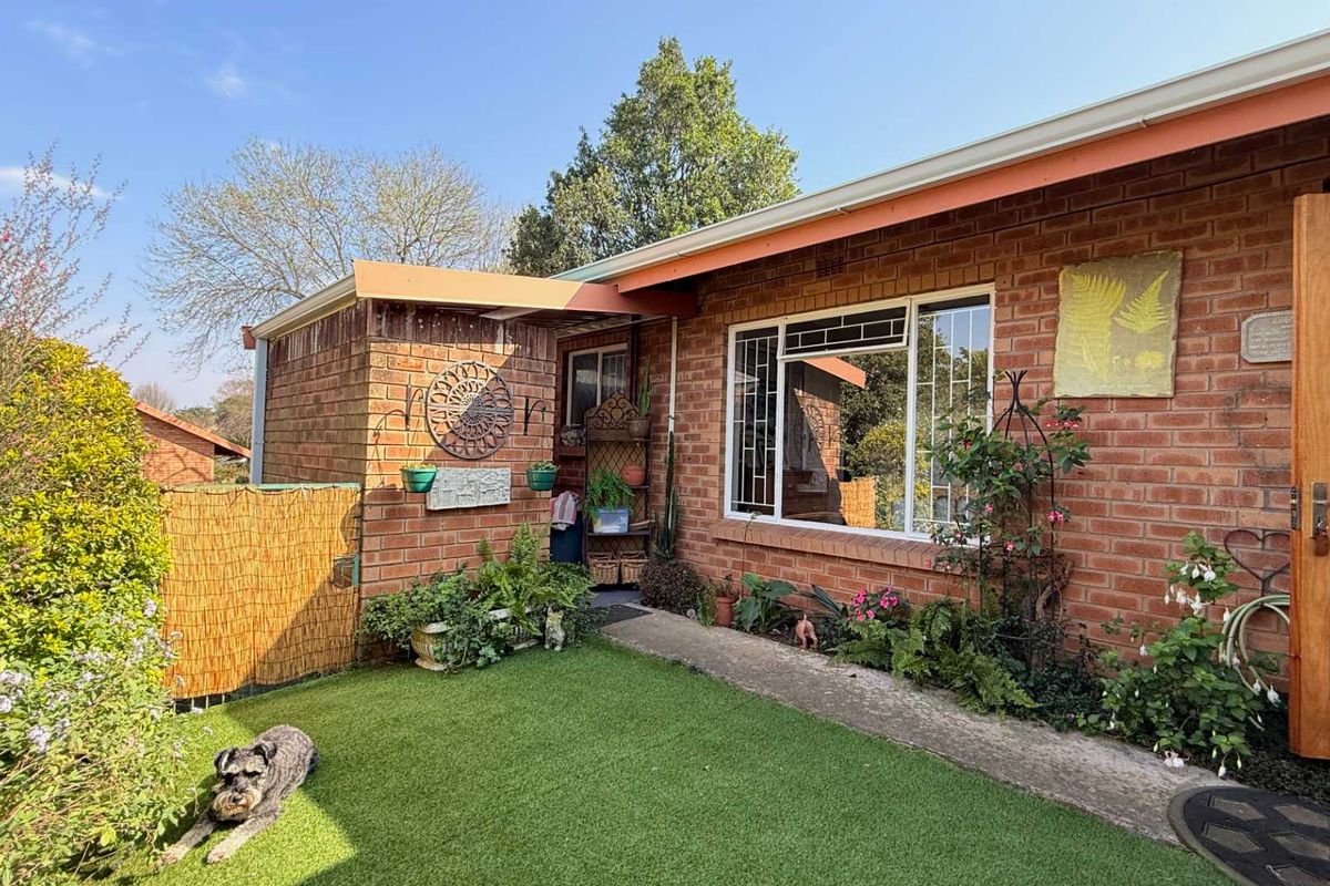 A rear exterior view of the townhouse featuring a brick facade, synthetic lawn, and a concrete walkway leading to a timber entrance door.