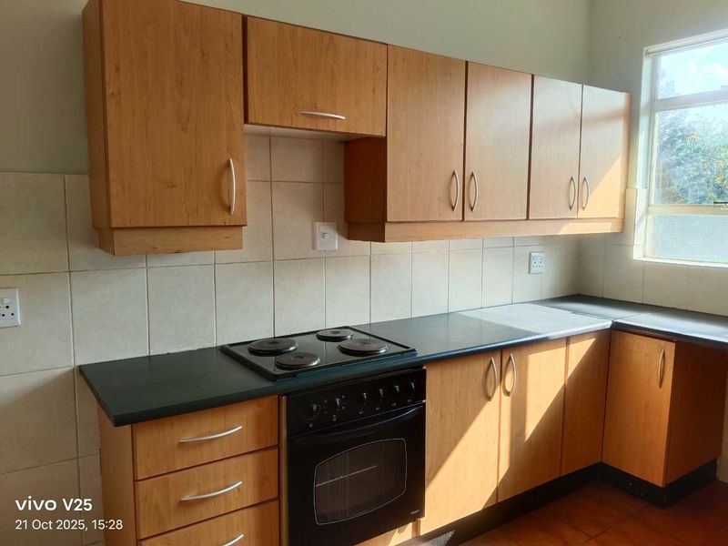 A functional kitchen featuring wooden cabinetry, a built-in oven with an electric hob, and a tiled backsplash.