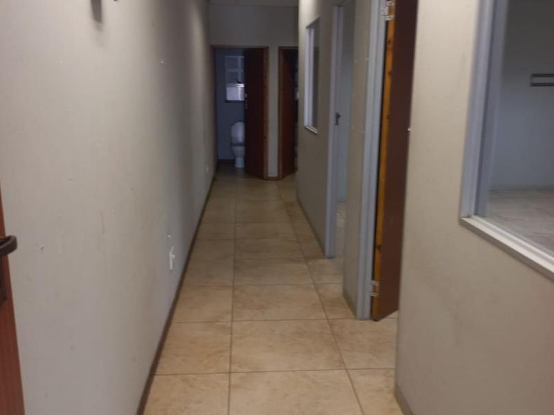 A functional office hallway featuring tiled flooring, suspended ceiling with recessed lighting, and access to multiple rooms including a restroom.