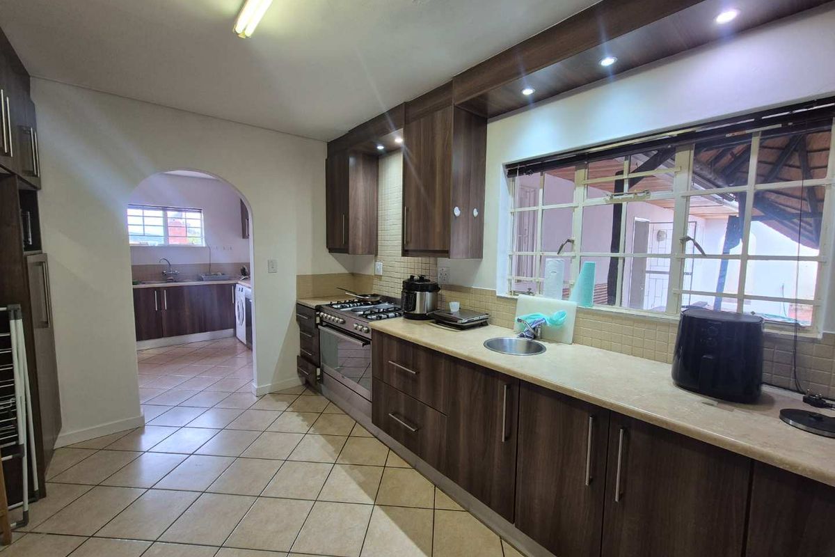 A functional kitchen featuring wood-finish cabinetry, tiled flooring, a built-in gas stove, and an arched doorway leading to a separate scullery area.