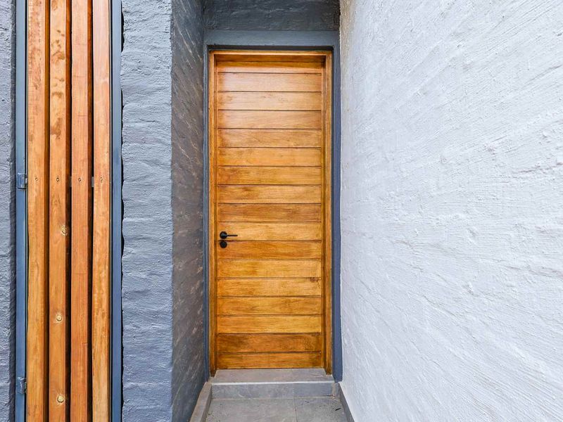 A modern entrance featuring a solid timber door, contrasting painted brick walls, and a decorative timber slat screen.