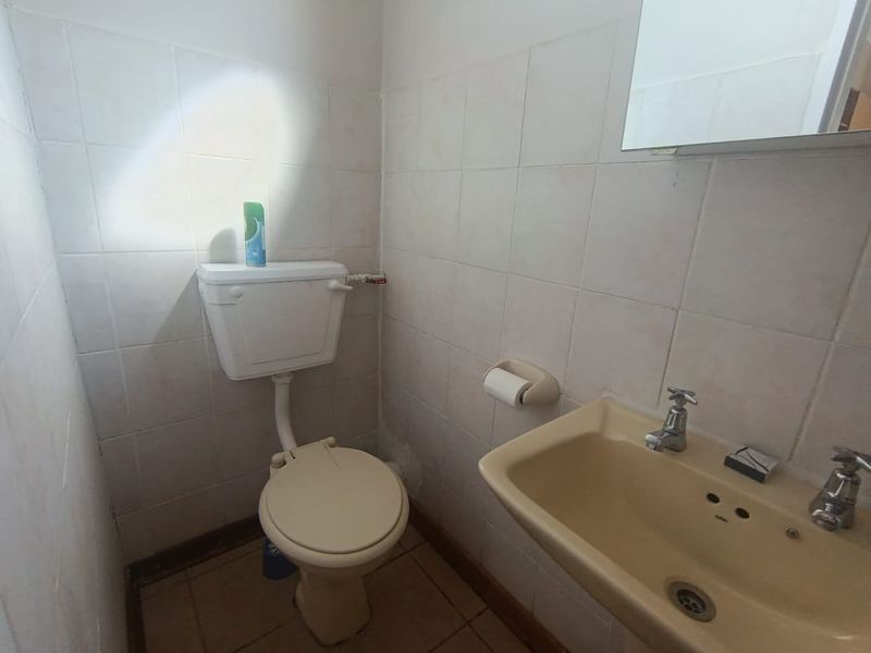 A compact guest bathroom featuring dated sanitaryware, ceramic wall tiling, and a wall-mounted mirror.