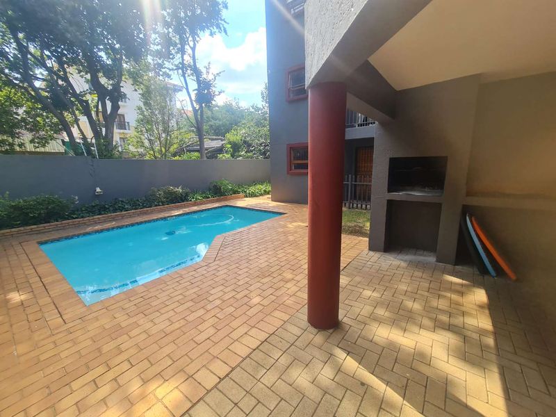 Outdoor entertainment area featuring a swimming pool, paved patio, and a built-in braai facility, perfect for relaxed outdoor living.