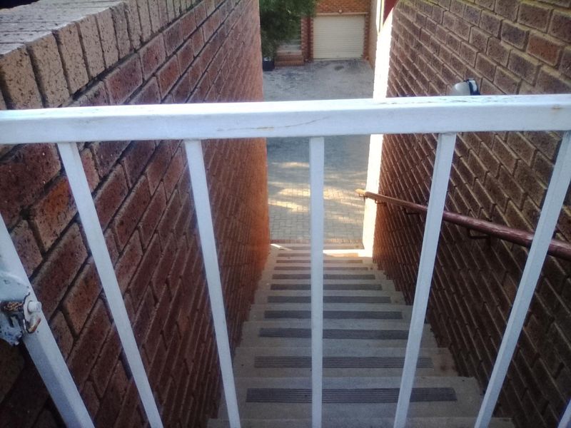 Exterior staircase with brick walls and metal railings leading down to a paved area and garage.