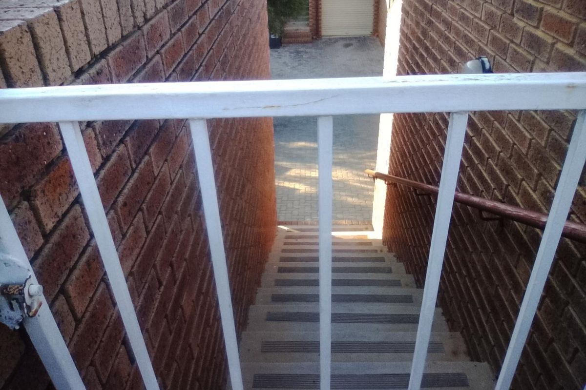 Exterior staircase with brick walls and metal railings leading down to a paved area and garage.