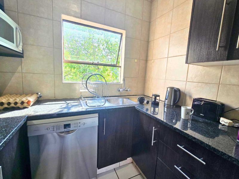 A functional kitchen featuring dark wood cabinetry, granite countertops, tiled backsplash, and integrated appliances including a dishwasher and microwave.