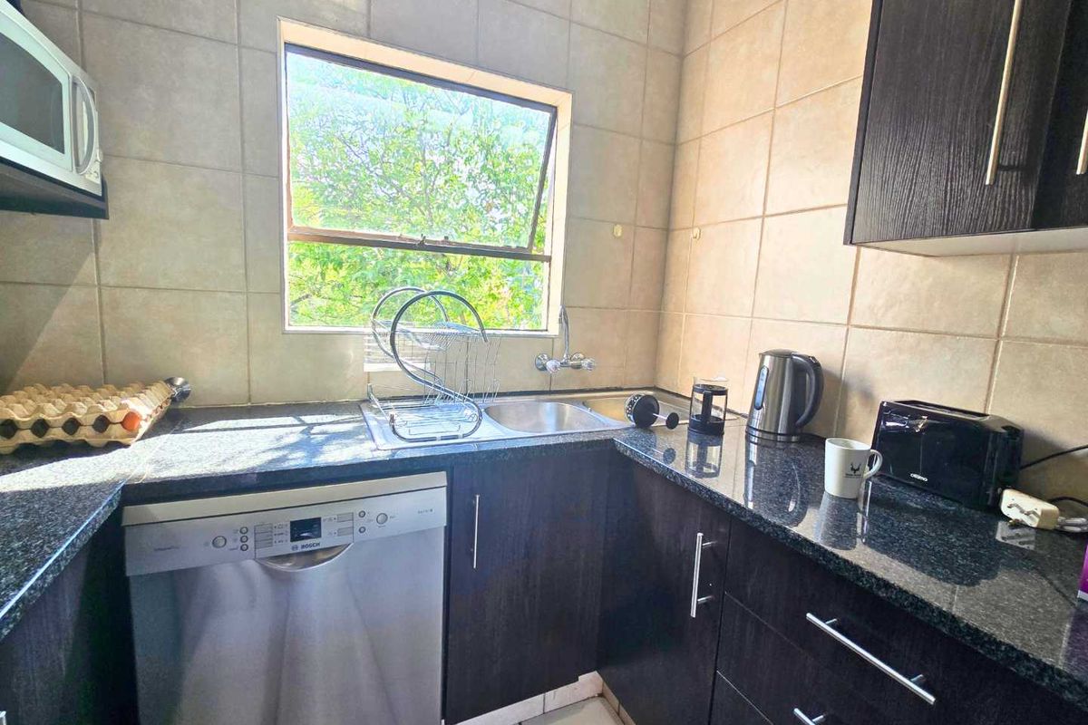 A functional kitchen featuring dark wood cabinetry, granite countertops, tiled backsplash, and integrated appliances including a dishwasher and microwave.