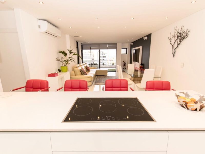Modern open-plan living area featuring a sleek kitchen island with integrated induction hob, recessed lighting, and seamless flow to the balcony.