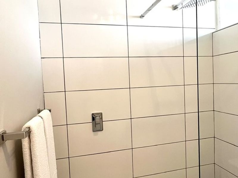 A modern walk-in shower featuring large format white wall tiles, a glass screen, and a rainfall shower head.
