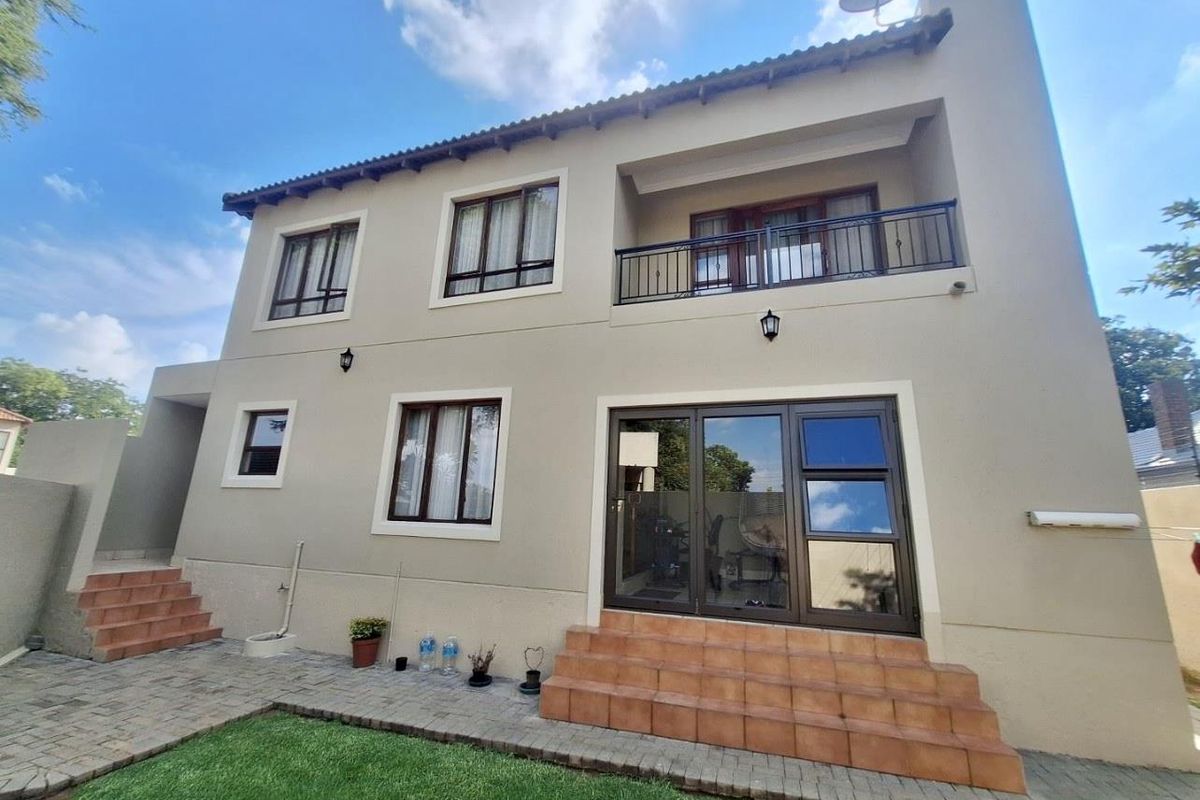 Rear view of a two-story townhouse featuring a paved patio, tiled entrance steps, balcony with metal railing, and well-maintained exterior walls.