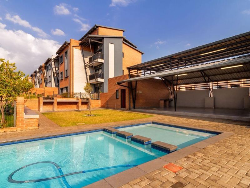 Communal outdoor area featuring a swimming pool, paved patio, and a covered entertainment space with a built-in braai facility.