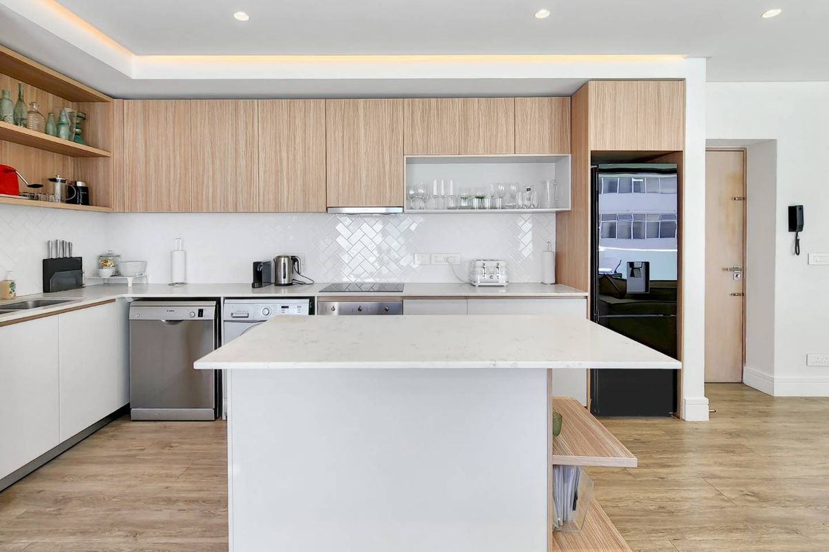 Modern kitchen featuring light wood cabinetry, white stone countertops, a central island, herringbone tile backsplash, and integrated appliances.