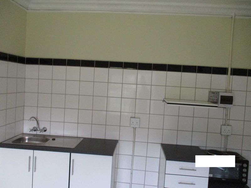 A functional kitchen area featuring white cabinetry, a stainless steel sink, and tiled splashbacks, providing a clean and practical space for culinary tasks.