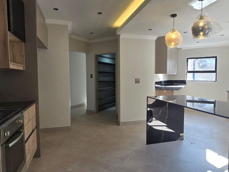 Modern kitchen featuring sleek cabinetry, stone countertops, integrated oven and hob, recessed lighting, and a spacious open-plan layout with tiled flooring.