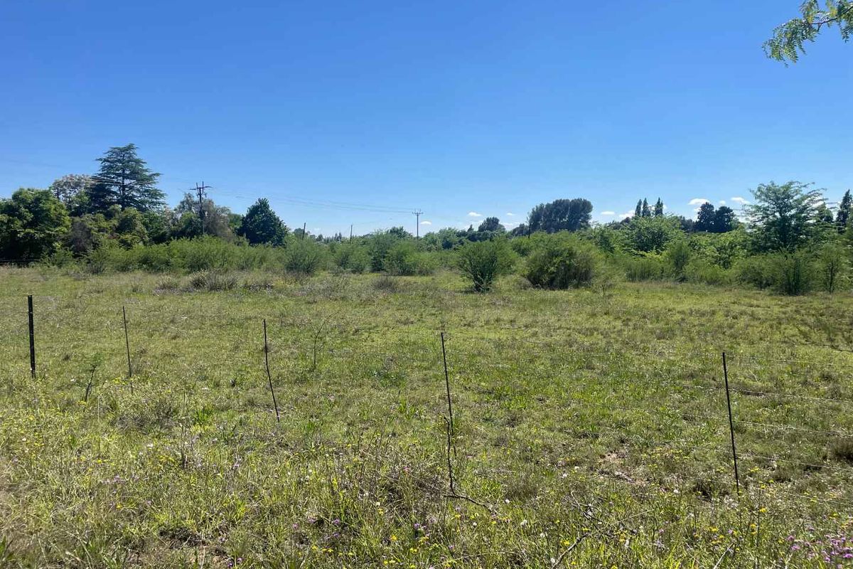 An expansive, undeveloped plot of land featuring natural vegetation and simple wire perimeter fencing, suitable for agricultural or residential development.