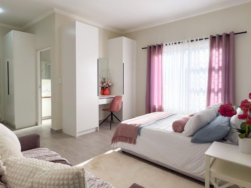 A well-maintained bedroom featuring built-in cupboards, a integrated vanity unit, tiled flooring, and neutral wall finishes with access to an en-suite bathroom.