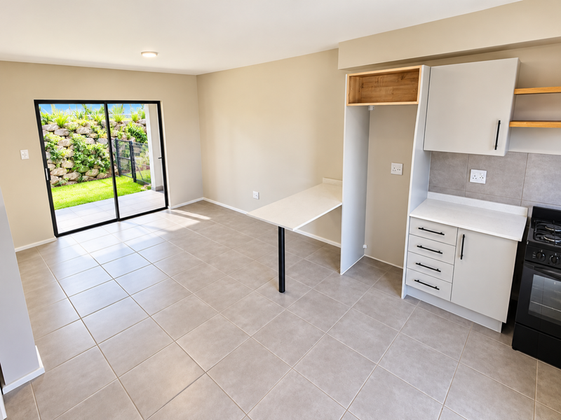 Modern open-plan kitchen and living area featuring neutral tiled floors, sleek cabinetry, and a sliding door leading to a private patio and garden.