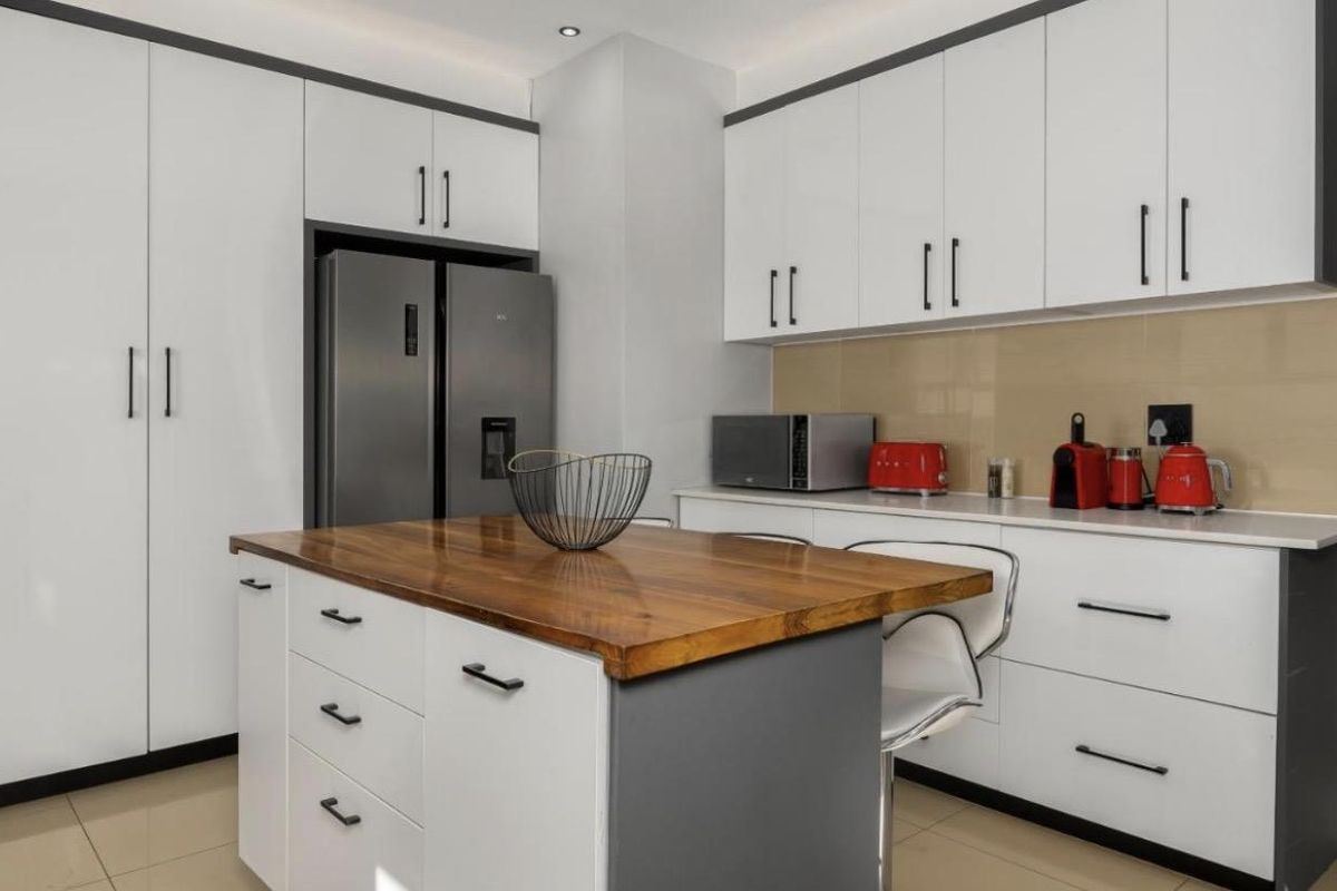 Modern kitchen featuring sleek white cabinetry, a central island with a wooden countertop, stone surfaces, and integrated storage solutions.