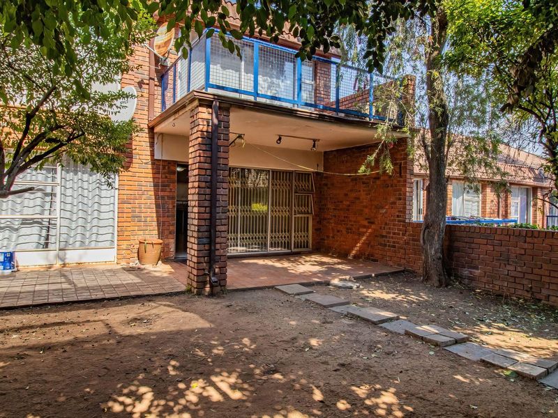 Rear view of the apartment featuring a covered patio, an upper-level balcony with metal railings, and a private garden area with brick boundary walls.