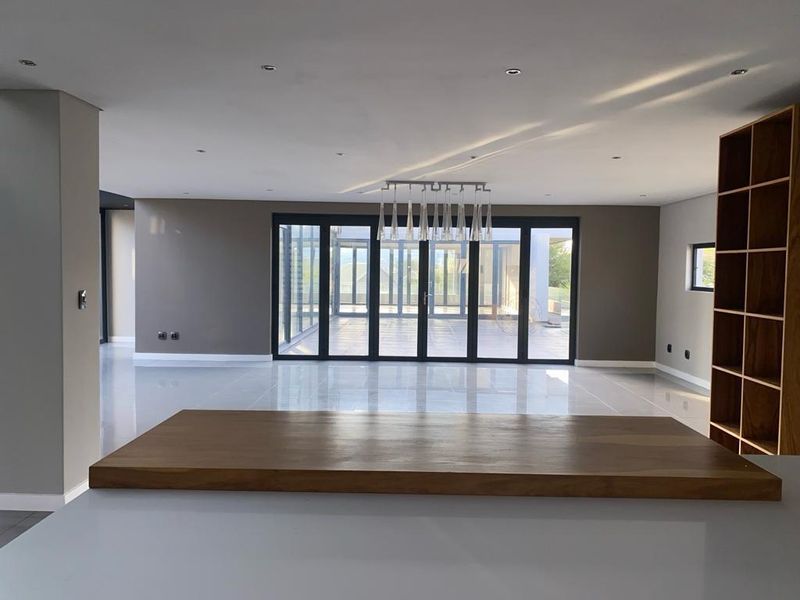 Spacious open-plan living area featuring large format floor tiles, built-in wooden shelving, and expansive glass sliding doors leading to an outdoor space.