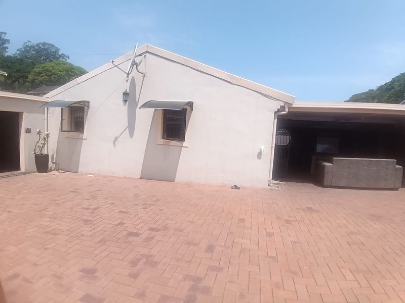 A rear exterior view of the property featuring a spacious brick-paved courtyard and a covered patio area.