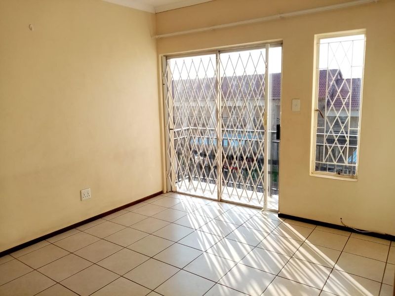 An empty living room featuring tiled flooring and a sliding glass door with a security gate, providing access to an outdoor area.