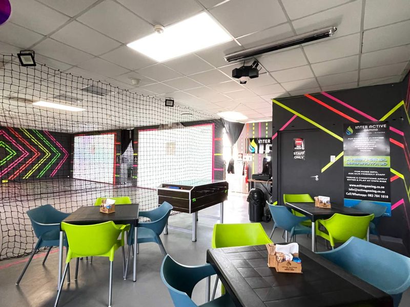 A vibrant indoor sports and gaming facility featuring durable vinyl flooring, suspended ceilings with recessed lighting, and protective safety netting for active play areas.