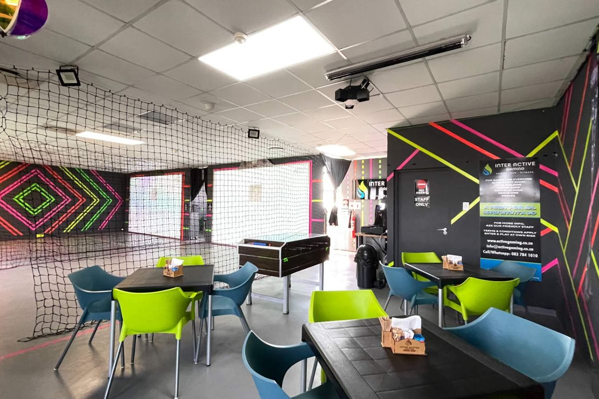 A vibrant indoor sports and gaming facility featuring durable vinyl flooring, suspended ceilings with recessed lighting, and protective safety netting for active play areas.